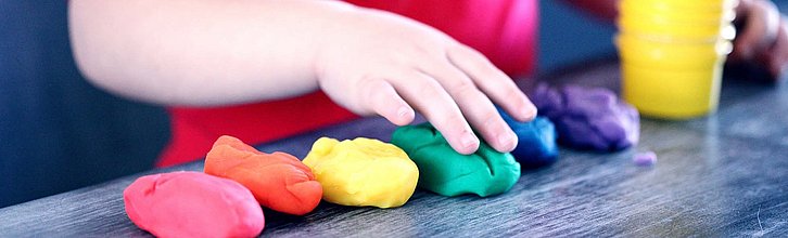Bunte Knethaufen auf einem Tisch, darüber eine Kinderhand.