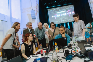 Mehrer Personen stehen um eine Person herum, die etwas auf einem Laptop zeigt.