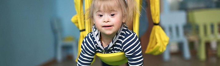 Kleines Kind mit Down Syndrom in einer Liege-Schaukel