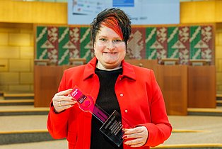 Eine Frau steht mit Preis in der Hand im Plenarsaal des NRW-Landtags.