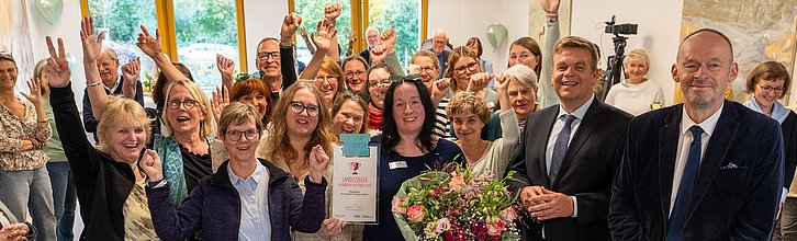 Jubelnde, glückliche Menschen. Eine Person hält einen Blumenstrauß und Urkunde in der Hand.