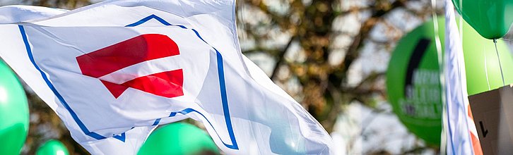 Flagge mit Paritätischem Gleicheitszeichen, die auf einer Demo geschwungen wird.