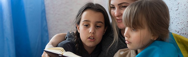 Frau liest zwei Kindern etwas vor