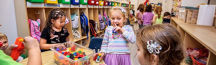 Gruppenraum einer Kita. Im Vordergrund spielen Kinder mit Bauklötzen.
