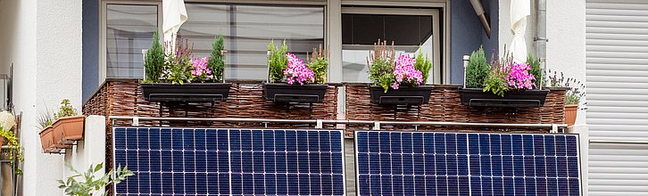Ein Balkon an einem Mehrfamilienhaushalt. Am Balkongeländer hängen Solarmodule.