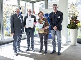 Vier Personen stehen für ein Foto lächelnd in einem Raum.