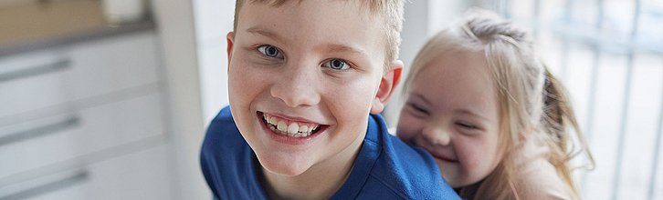 Ein Junge und ein Mädchen mit Behinderung raufen miteinander und lächeln vergnügt in die Kamera.