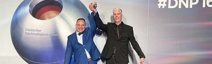 Zwei jubelnde Personen stehen mit Deutschen Nachhaltigkeitspreis in der Hand auf einer Bühne.