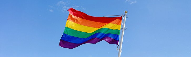 Regenbogenflagge weht vor blauem Himmel am Fahnenmast im Wind