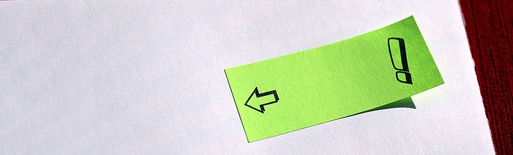 Notizzettel mit Ausrufezeichen klebt auf einem Blatt Papier.