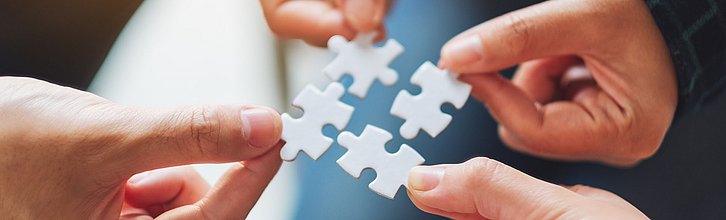 Vier Hände, die vier passende Puzzleteile aneinanderhalten.