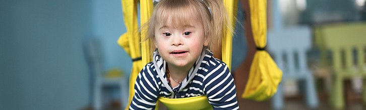 Ein Kind mit Down-Syndrom in einer Therapieschaukel.