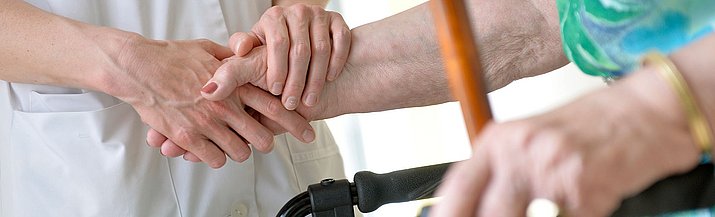 Eine Pflegerin hälft die Hand einer älteren Dame am Rollator
