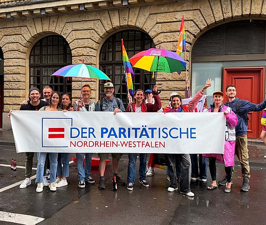 Viele Personen versammelt hinter einem Banner mit Logo des Paritätischen NRW