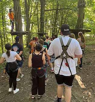 Jugendliche erhalten eine Klettereinweisung in einem Waldkletterpark während der Jubiläumsfeier der Ombudschaft Jugendhilfe NRW.