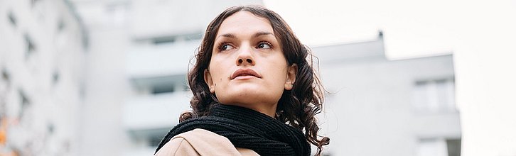 Eine Person mit langen, braunen Haaren steht vor einem Häuserblog