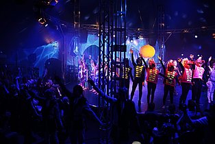 Zirkusbühne mit Kindern in Kostümen und einem klatschendem Publikum.