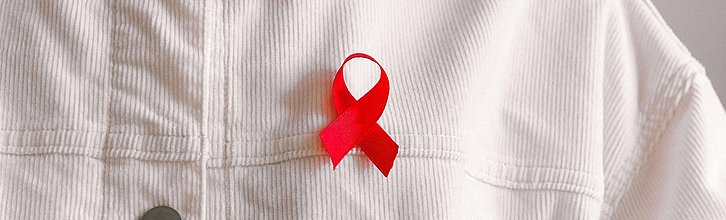 Weiße Cordjacke mit roter Aids-Schleife als Anstecker.