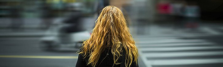 Eine Frau mit langen Haaren überquert eine Straße.