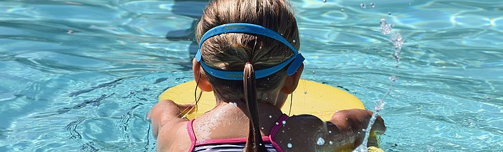 Ein Kind von hinten das mit einem Schwimmreifen schwimmt.