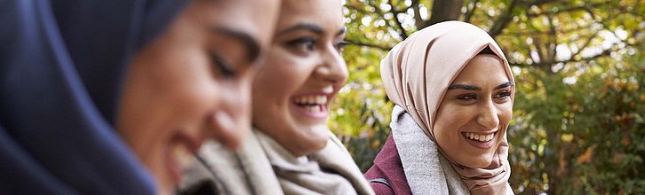 Drei Frauen, die Kopftuch tragen, stehen nebeneinander und lächeln.