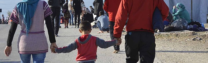 Eine Familie läuft Hand in Hand durch ein Flüchtlingslager.