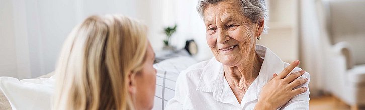 Pflegekraft legt Hand auf die Schulter einer Seniorin