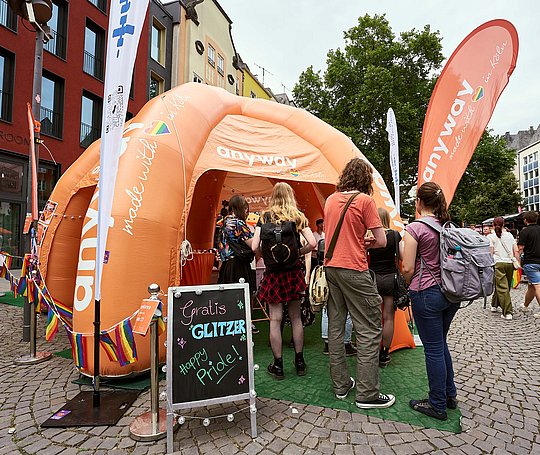 Orangfarbener Pavillon mit anyway-Schriftzug. Eine Schlange mit wartenden Menschen davor.