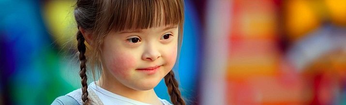 Ein Mädchen mit Down-Syndrom vor einem bunten Hintergrund.
