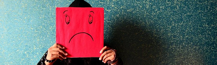 Person hält ein Schild mit einem gemalten negativen Gesicht vor das Gesicht