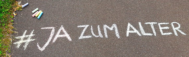 Aktionstag-Slogan "Ja zum Alter" mit Kreide auf eine Gehweg gemalt.