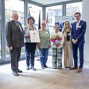 Sechs Personen stehen für ein Foto lächelnd in einem Raum