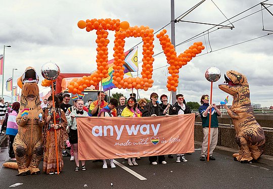 Menschenmenge, die hinter einem anyway-Banner läuft und das Wort "Joy" aus Luftballons trägt.