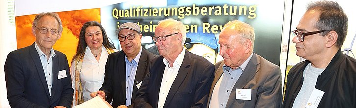 Sechs Personen stehen an einem Beratungstisch.