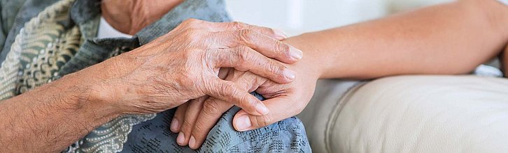 Die Hand einer jungen Person liegt fürsorglich auf der Schulter einer älteren Person. Die älter Person legt ihre Hand auf die Hand.
