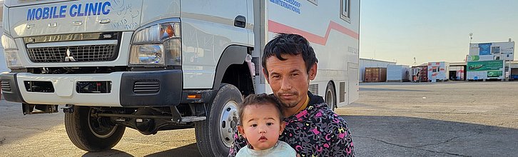 Eine erwachsene Person mit Kind sitz vor einem LKW mit Aufschrift "Mobile Clinic".