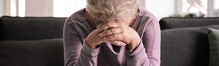 Ältere Frau stützt Hände auf den Kopf und schaut nach unten