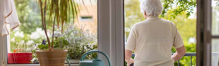 Eine Seniorin steht auf ihrem Balkon.