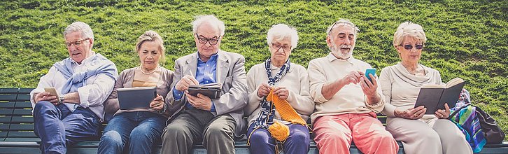 Sechs Senior*innen sitzen auf einer Bank und üben verschiedene Aktivitäten aus.