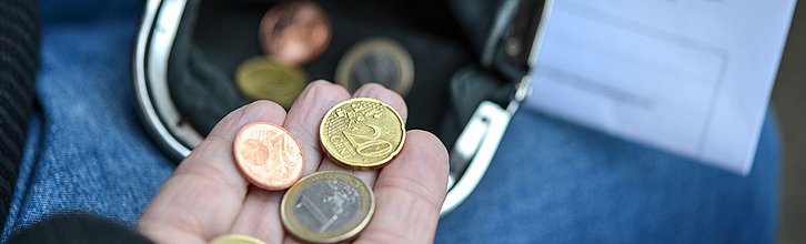 Eine Hand, die ein paar Münzen in ein Portmoinee schüttet.