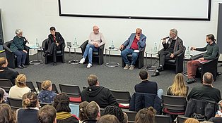 Ein Hörsaal mit vielen Menschen, die den sechs Menschen auf der Bühen beim diskutieren zugucken.