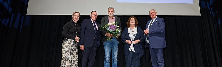 Fünf Personen auf einer Bühen. In der Mitte Gewinner Andreas Fuhrmann mit Blumenstrauß.