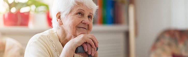 Eine ältere Frau mit einer Gehhilfe sitzt in einem Sessel.