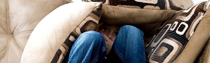 Ein Kind sitzt auf einem Sofa und versteckt sich unter Kissen.